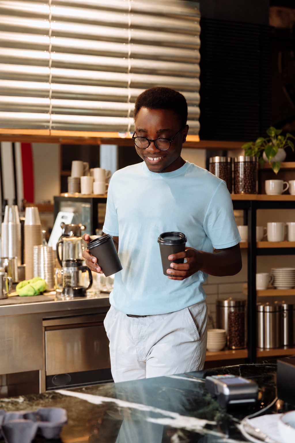 En smilende mannlig kaféansatt holder to kaffekopper ved disken